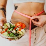 Woman holding a vegetable salad while measuring her waist with a tape measure, healthy weight loss concept