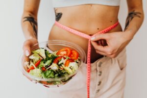 Woman holding a vegetable salad while measuring her waist with a tape measure, healthy weight loss concept