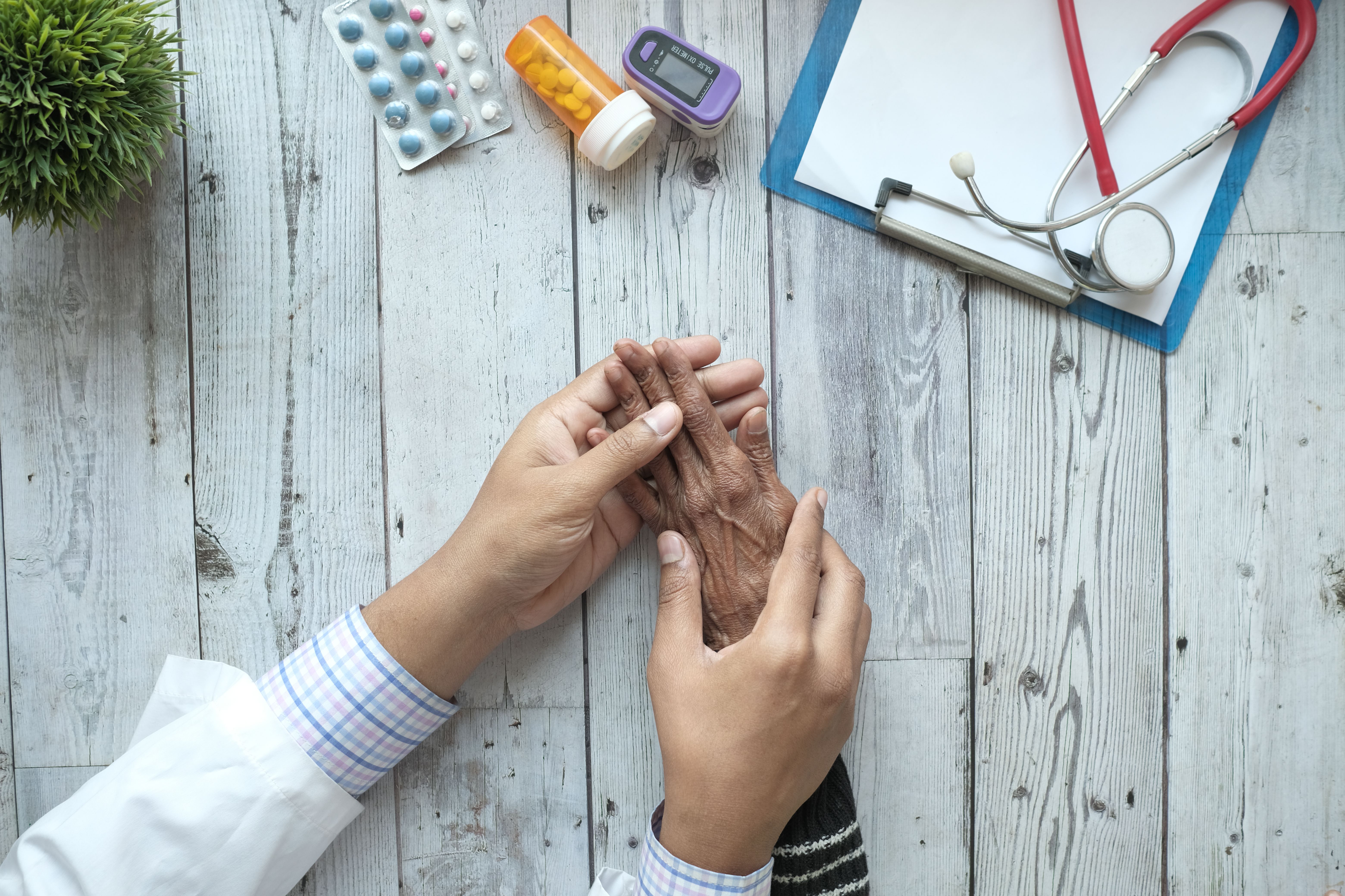 Doctor holding elderly patient hands with medication and stethoscope